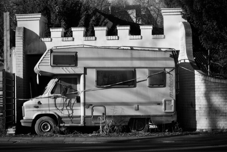 carado - A vintage camper van parked beside a brick wall, showcasing abandonment and decay in a mono