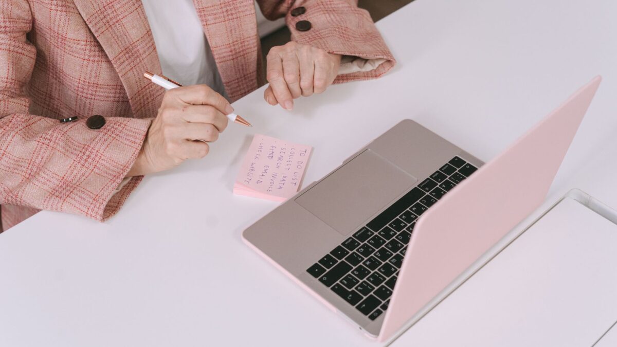 Person vergleicht am Schreibtisch Produktangaben auf dem Laptop mit eigenen Notizen